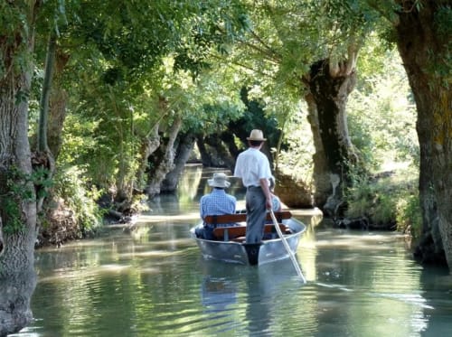 Deux hommes ramant dans une barque sur une voie navigable bordée d'arbres près du Petit Moulin à Pouzauges