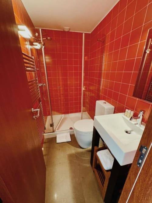 Banheiro moderno com azulejos vermelhos, chuveiro aberto, pia e toilet brancos na Quinta Trindade em Arouca