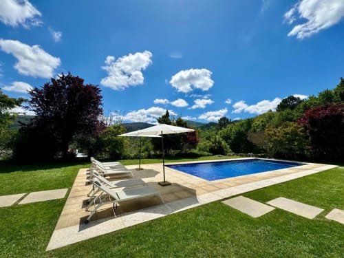 Área de piscina Quinta Trindade com espreguiçadeiras, guarda-sol e vistas para as montanhas em Arouca, Portugal