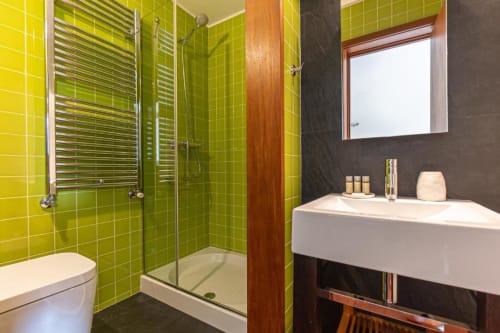 Banheiro moderno na Quinta Trindade com azulejos verde-limão, box de vidro, pia branca e paredes de destaque escuras
