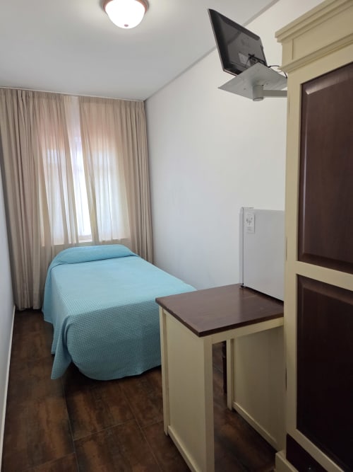 Habitación individual en Hostal Atalaya, Minas de Riotinto: cama azul, escritorio, TV y ventana con cortinas beige