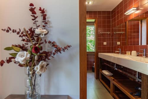 Casa de banho moderna da Quinta Trindade com azulejos vermelhos, flores brancas em vaso, lavatório e janela com vista para o jardim em Arouca