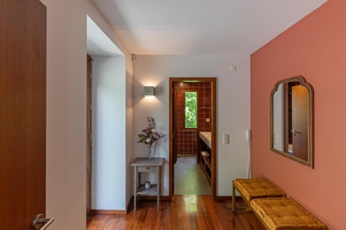Corredor da Quinta Trindade com parede de destaque coral, piso de madeira, espelho e móveis elegantes
