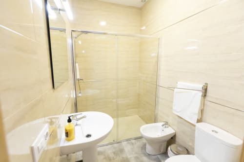 Baño moderno con cabina de ducha cristal, lavabo pedestal y toallero blanco en Hostal Restaurante Atalaya de Minas de
