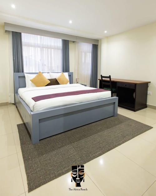 Modern studio apartment at The Africa Reach in Accra with gray bed, yellow pillows, desk, and floor-to-ceiling windows with