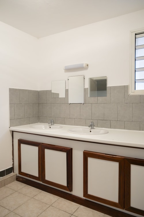 Salle de bain moderne à Mamoudzou avec double vasque, crédence en carrelage beige et meuble sous-vasque en bois