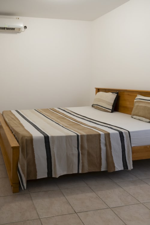 Lit en bois avec literie rayée blanc, beige et charbon dans la chambre lumineuse de l'hôtel NGAYABE 976, Mamoudzou