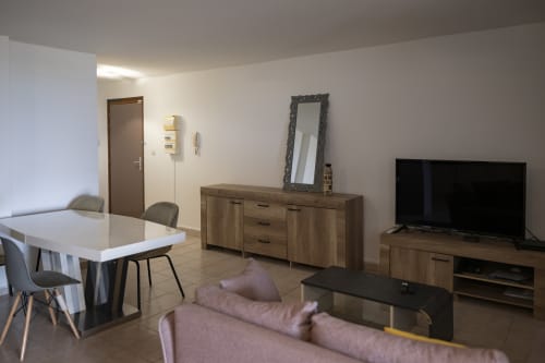 Intérieur d'appartement moderne à Mamoudzou avec salle à manger, salon meublé, TV, commode avec miroir et carrelage