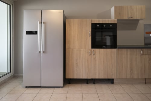 Cuisine moderne avec réfrigérateur blanc côte à côte et mobilier en bois, four noir à l'appartement NGAYABE 976 à Mamoudzou