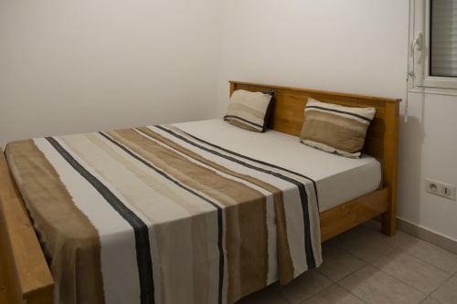 Lit en bois avec literie rayée et oreillers dans l'appartement CP204 à NGAYABE 976, Mamoudzou