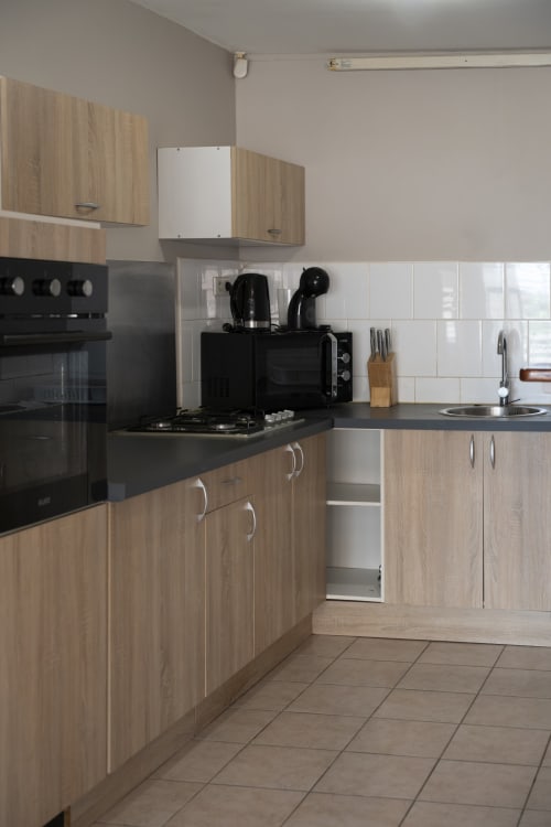 Cuisine moderne de l'appartement CP204 à NGAYABE 976, Mamoudzou avec placards en bois, plan de travail noir et carrelage blanc