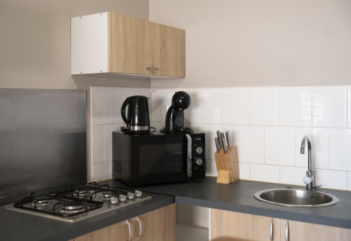 Cuisine moderne de l'appartement NGAYABE 976 avec cuisinière à gaz, micro-ondes noir, bouilloire, bloc de couteaux et carrelage blanc métro