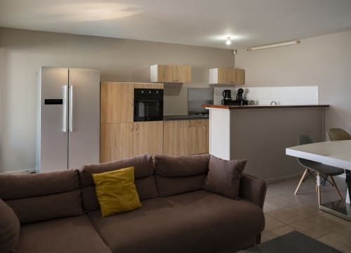 Appartement moderne ouvert à Mamoudzou avec canapé sectionnel marron, cuisine en bois et électroménagers inoxydable