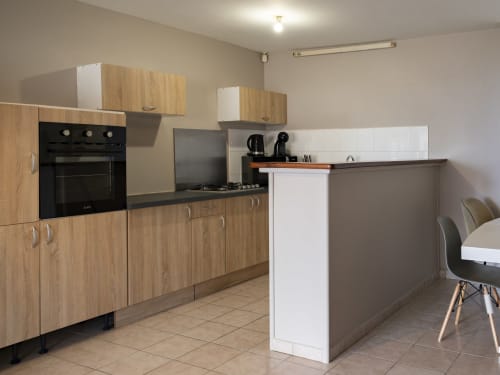 Cuisine moderne de l'appartement NGAYABE 976 avec meubles en bois, four noir, îlot central et coin repas à Mamoudzou