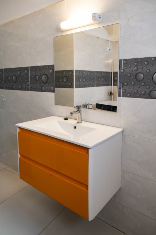 Meuble de salle de bain moderne avec façade orange, lavabo blanc et miroir à l'appartement NGAYABE 976 à Mamoudzou