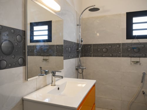 Salle de bains moderne à NGAYABE 976 à Mamoudzou avec carrelage crème et foncé, douche vitrée, lavabo blanc et chromé