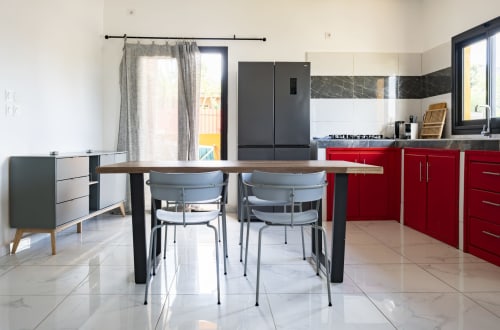 Cuisine-séjour moderne de l'appartement NGAYABE 976 à Mamoudzou avec mobilier rouge, plan en marbre et table en bois