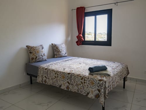 Chambre accueillante à NGAYABE 976 à Mamoudzou avec literie motifs, coussins décoratifs et fenêtre vue ville bordeaux