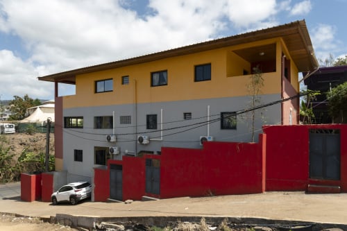 Résidence NGAYABE 976 à Mamoudzou, façade jaune et grise, clôture rouge, balcons avec vue sur la ville