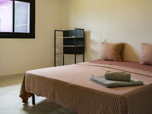 Chambre de l'appartement NGAYABE 976 à Mamoudzou avec literie à carreaux, étagère et fenêtre avec vue sur la ville