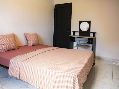 Chambre cosy de l'appartement NGAYABE 976 à Mamoudzou avec literie à carreaux rouges, porte noire, bureau avec miroir et bois clair