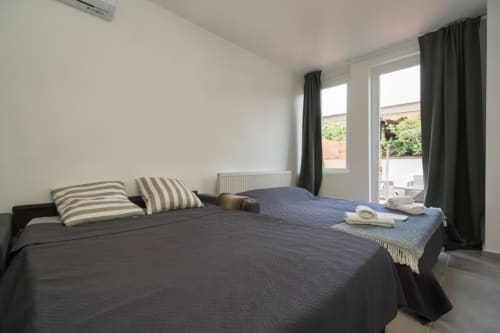Camera da letto moderna nell'appartamento di Rozzano con letto matrimoniale, cuscini rigati, biancheria scura e porte-finestre che si aprono sul balcone