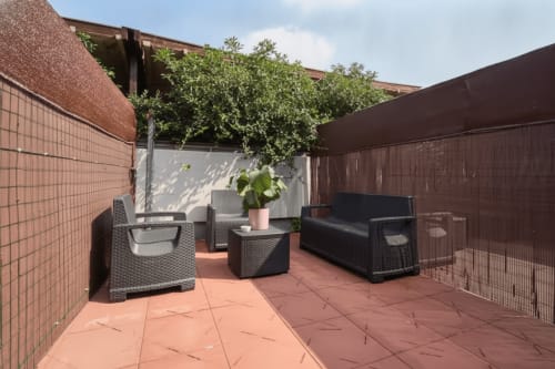 Terrazza soleggiata sul tetto dell'appartamento AirFlat Yellow House a Rozzano con mobili in vimini nero, piante in vaso e mattoni