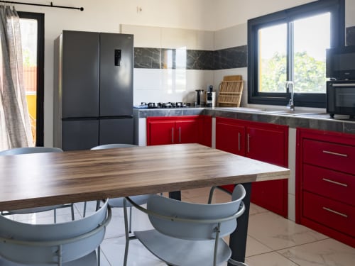 Cuisine moderne aux armoires rouges, électroménagers noirs, table à manger en bois et grandes fenêtres de l'appartement NGAYABE 976