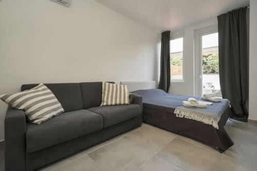 Moderno monolocale a Rozzano con divano scuro e letto blu, tende grigie e ampie finestre