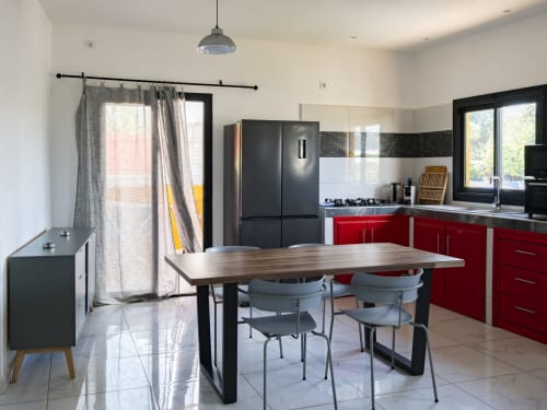 Cuisine-salle à manger moderne dans un appartement de Mamoudzou avec armoires rouges, réfrigérateur noir, table à manger et portes vitrées coulissantes vers