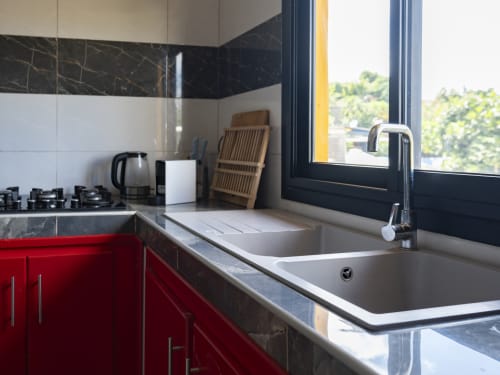 Cuisine moderne avec armoires rouges, évier en acier inoxydable, dosseret en marbre noir, cuisinière à gaz et grandes fenêtres avec vue