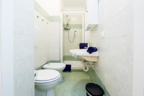 Bagno moderno nell'appartamento La Superba Stay Genova con toilette, bidet, lavabo e box doccia con dettagli in piastrelle verdi