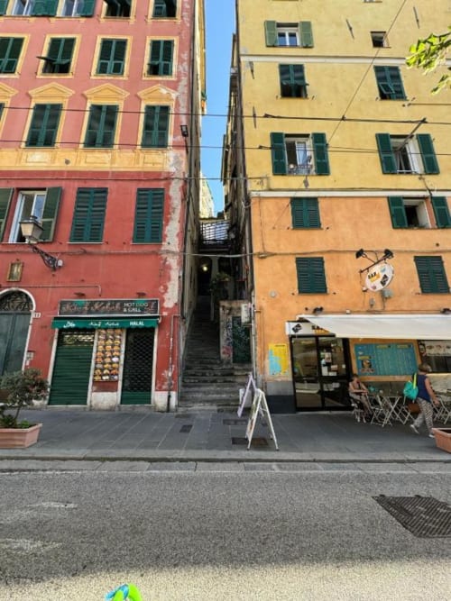 Edifici storici colorati su una stretta via genovese con piccoli negozi e appartamenti presso La Superba Stay hotel