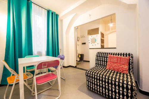 Zona living dell'appartamento Balbi a La Superba Stay Genova con scrivania, divano nero decorato, tende turchesi e angolo cucina moderno