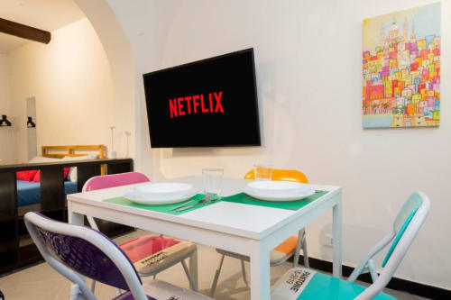 Moderna sala da pranzo dell'appartamento Balbi a La Superba Stay Genova con tavolo bianco, sedie colorate, Netflix sulla TV e cucina