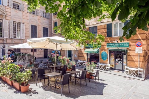 Cortile esterno della La Superba Stay Genova con tavoli da pranzo, ombrelloni e edifici storici ricoperti di edera a Genova