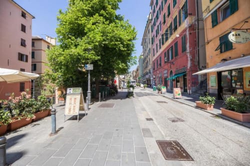 Affascinante via lastricata a Genova con edifici storici colorati, tavoli all'aperto e botteghe vicino a La Superba Stay