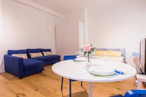 Area soggiorno del monolocale a Genova con divano blu, tavolo da pranzo bianco e letto presso La Superba Stay
