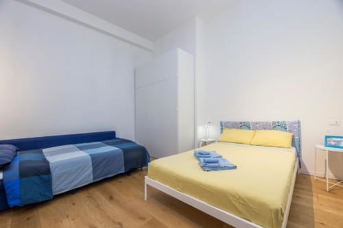 Camera luminosa dello studio apartment La Superba Stay Genova con letti gialli e blu, pavimenti in legno e comfort moderni