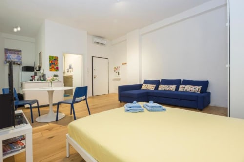 Luminoso monolocale a La Superba Stay Genova con letto giallo, divano blu scuro, angolo cottura e pavimenti in legno