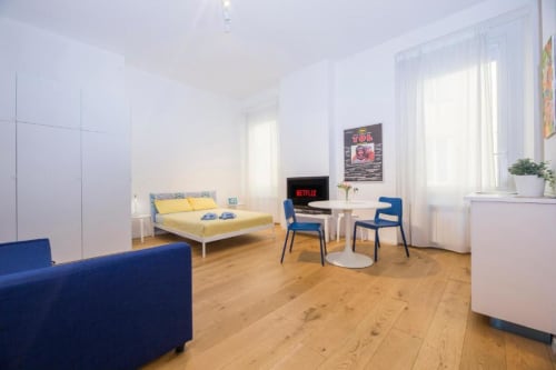 Moderno monolocale a La Superba Stay Genova con letto giallo, divano blu, zona pranzo e angolo cottura su parquet
