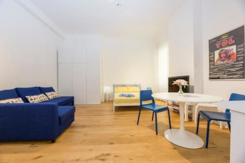 Moderno monolocale a Genova con divano blu, letto giallo, tavolo da pranzo bianco e pavimento in legno
