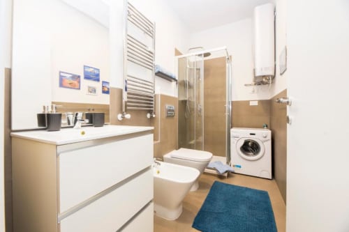 Moderno bagno nello studio La Superba Stay Genova con doccia, toilette, lavabo, lavatrice e tappeto blu
