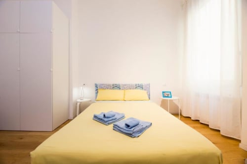 Camera da letto luminosa a La Superba Stay Genova con biancheria gialla, asciugamani blu, pavimenti in legno e armadio.