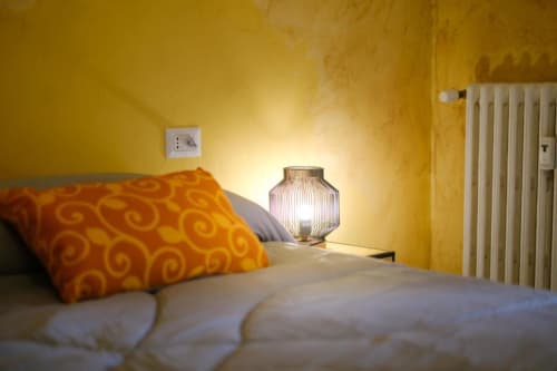 Accogliente camera di Casa Aurora Room Klimt a Rozzano con pareti gialle, cuscino con motivi arancioni e lampada decorativa