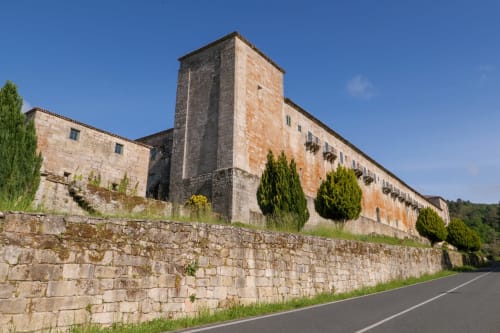 Exterior del hotel Casiña D'Avoa en Osera con muros de piedra, torre y cipreses bajo cielo azul