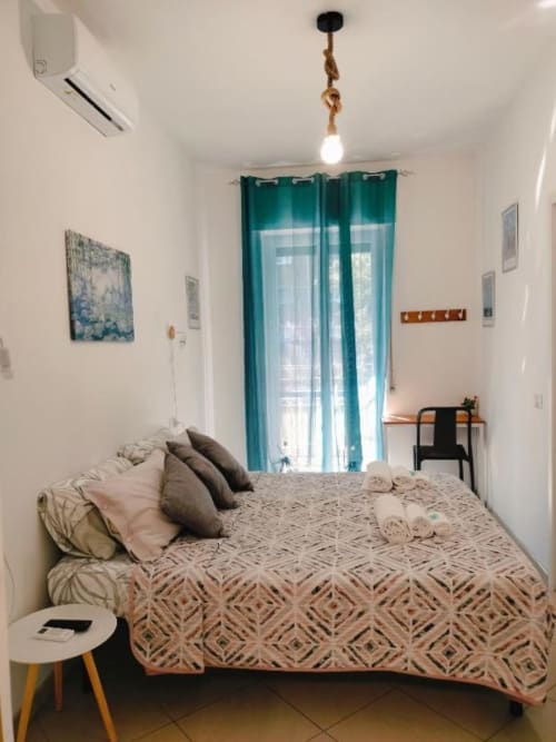 Camera luminosa all'Affittacamere Rozzano con letto, tende azzurre, lampadario moderno e arredamento contemporaneo
