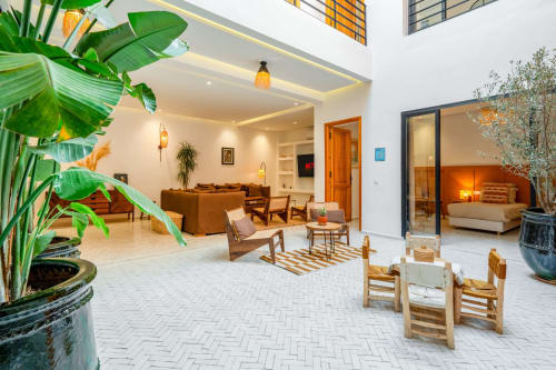 Modern open-plan living area at M Résidences et Hôtels with tropical plants, wooden furniture, and bedroom suite visible