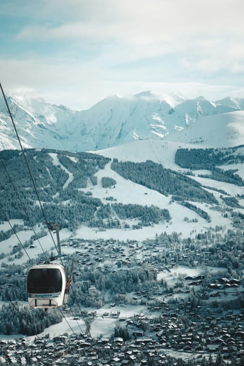 Téléphérique des Résidences M montant vers les sommets alpins enneigés au-dessus d'un village de montagne français en hiver