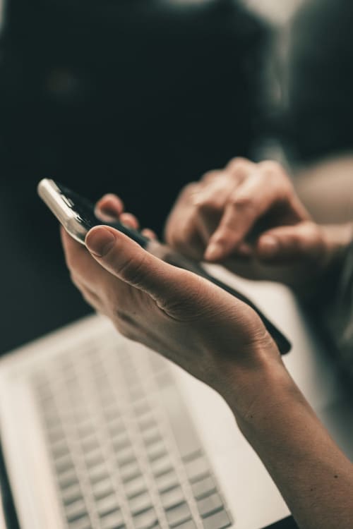 Personne tenant un smartphone avec un ordinateur portable, gestion immobilière M Résidences et Hôtels